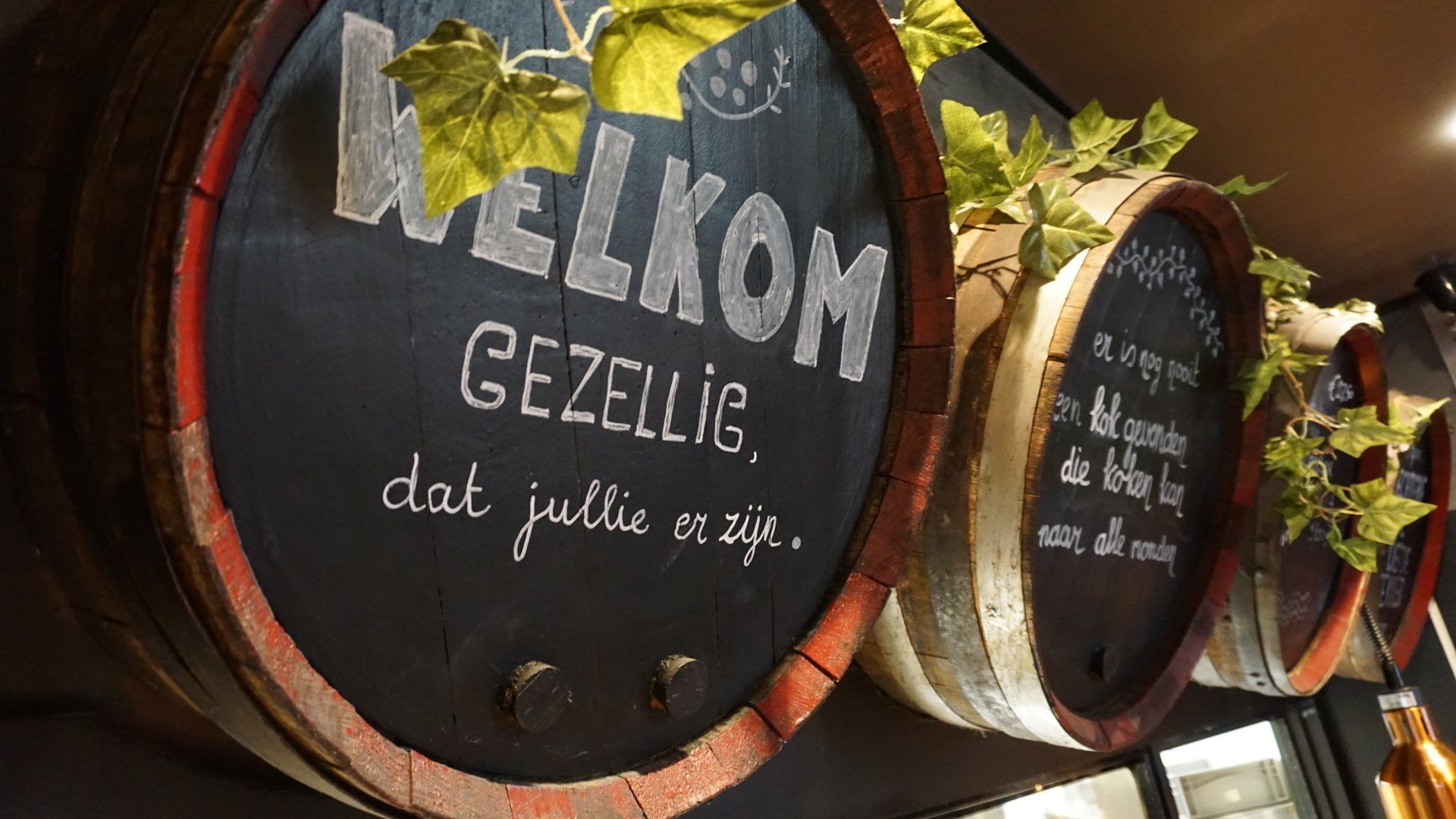 Rustieke houten tonvormige borden met Nederlandse welkomsttekst en groene planten in een winkelvitrine.