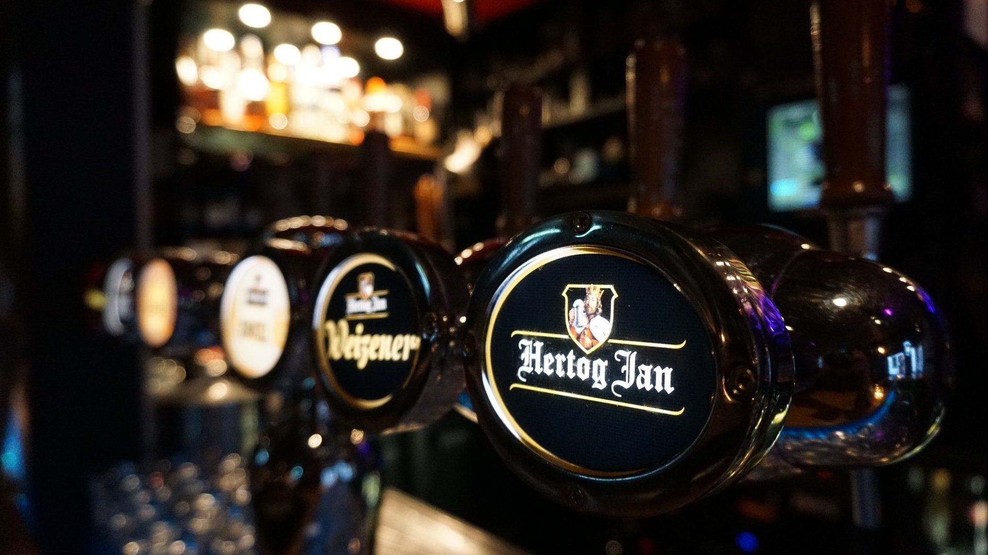 Een rij Hunterian-biertaps in een schemerig verlichte bar, met glanzende zwarte hendels en gouden accenten.