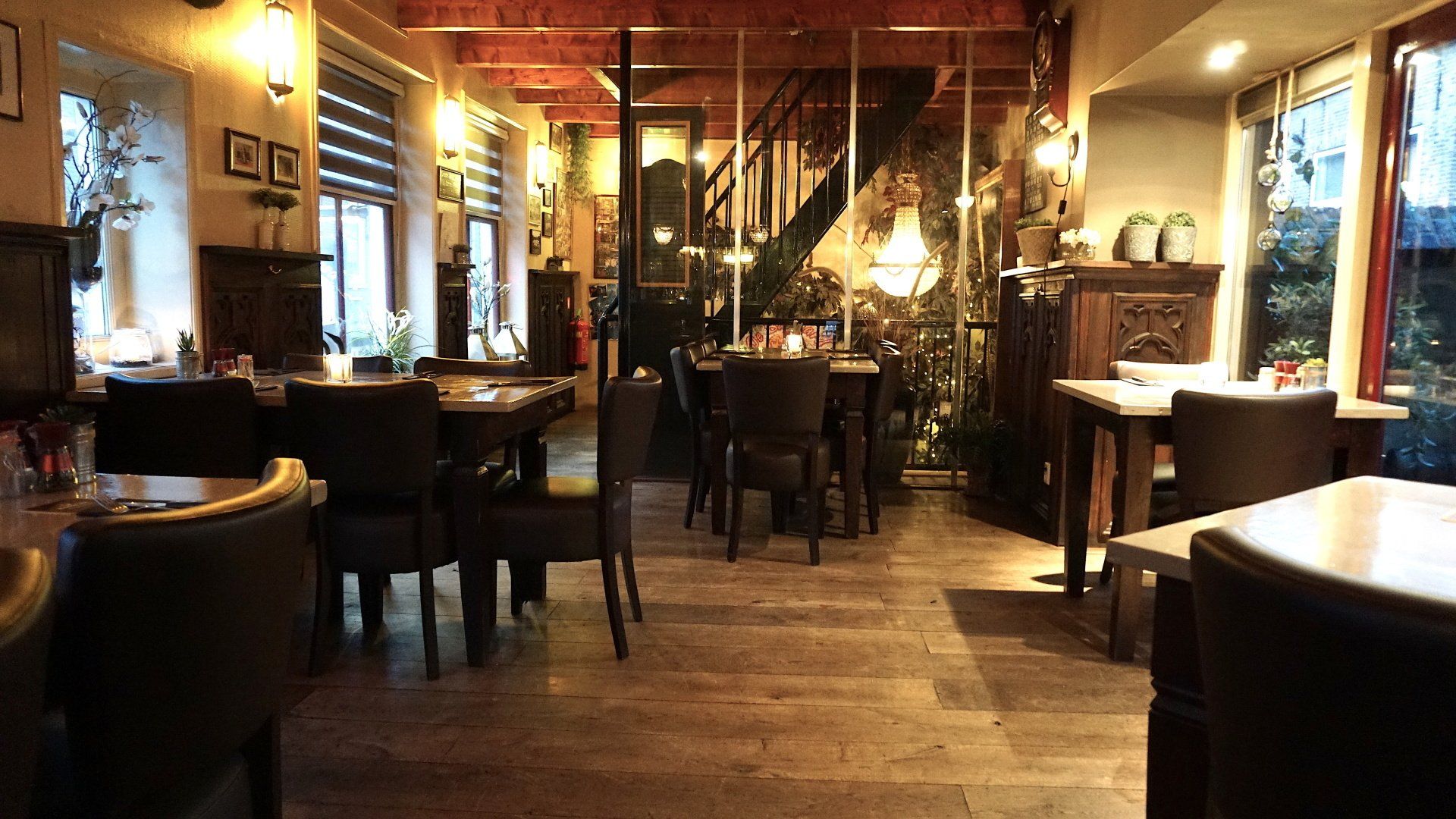 Gezellig restaurantinterieur met houten tafels, warme verlichting en bakstenen muren.