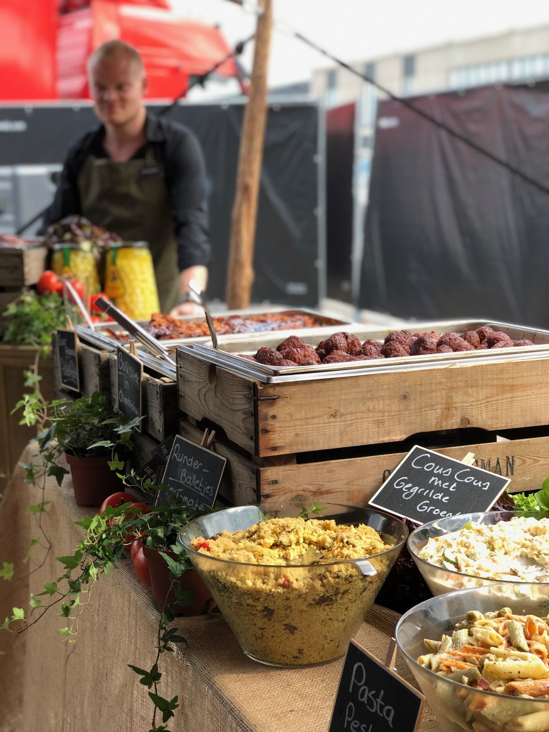 Marktkraam met diverse gebakjes en groenten en fruit in manden en schalen, met een verkoper achter de uitstalling.