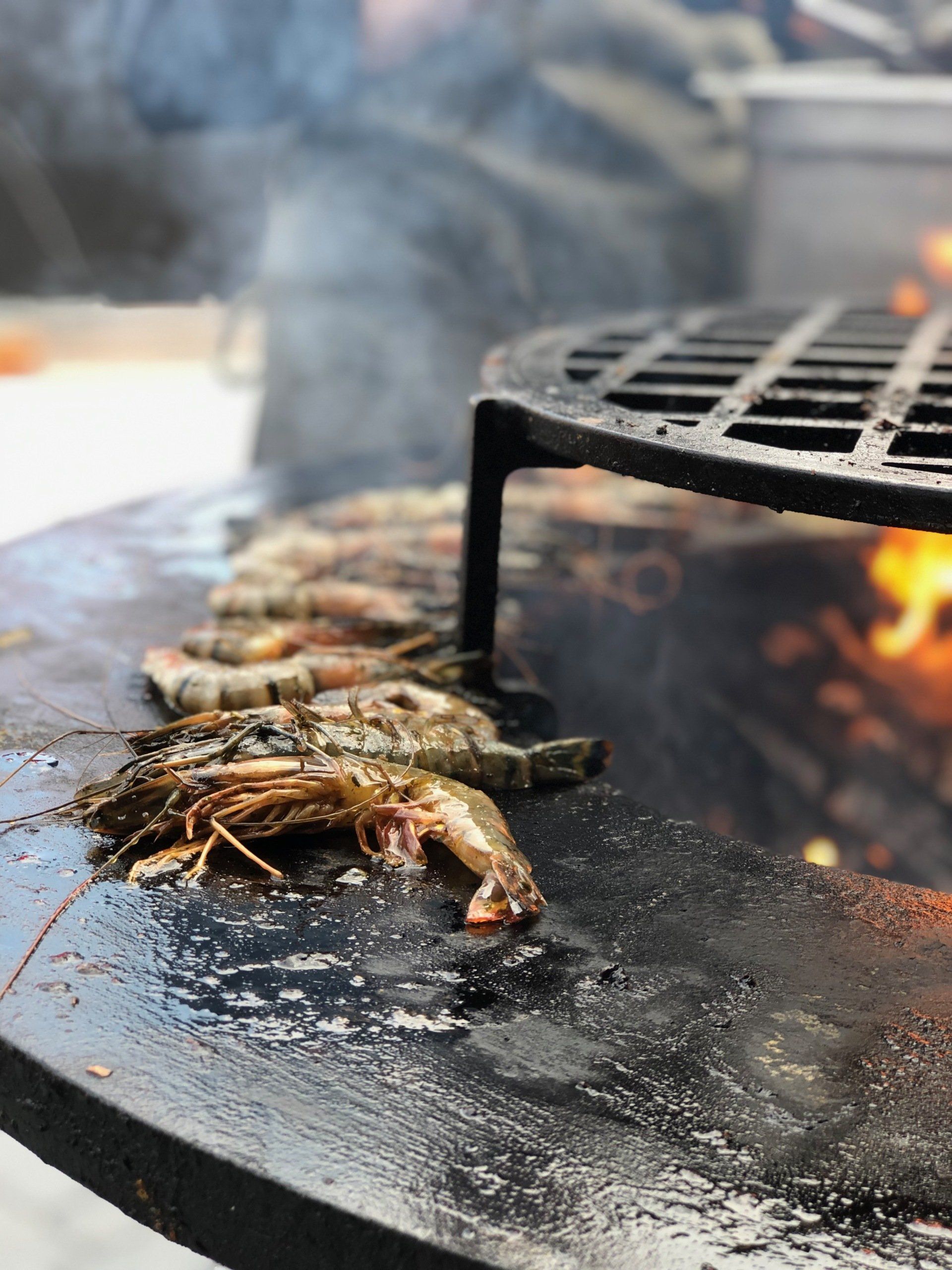 Zeevoedsel gegrild op een rokerige barbecue, met garnalen en vis op een zwarte bakplaat vlakbij open vuur.