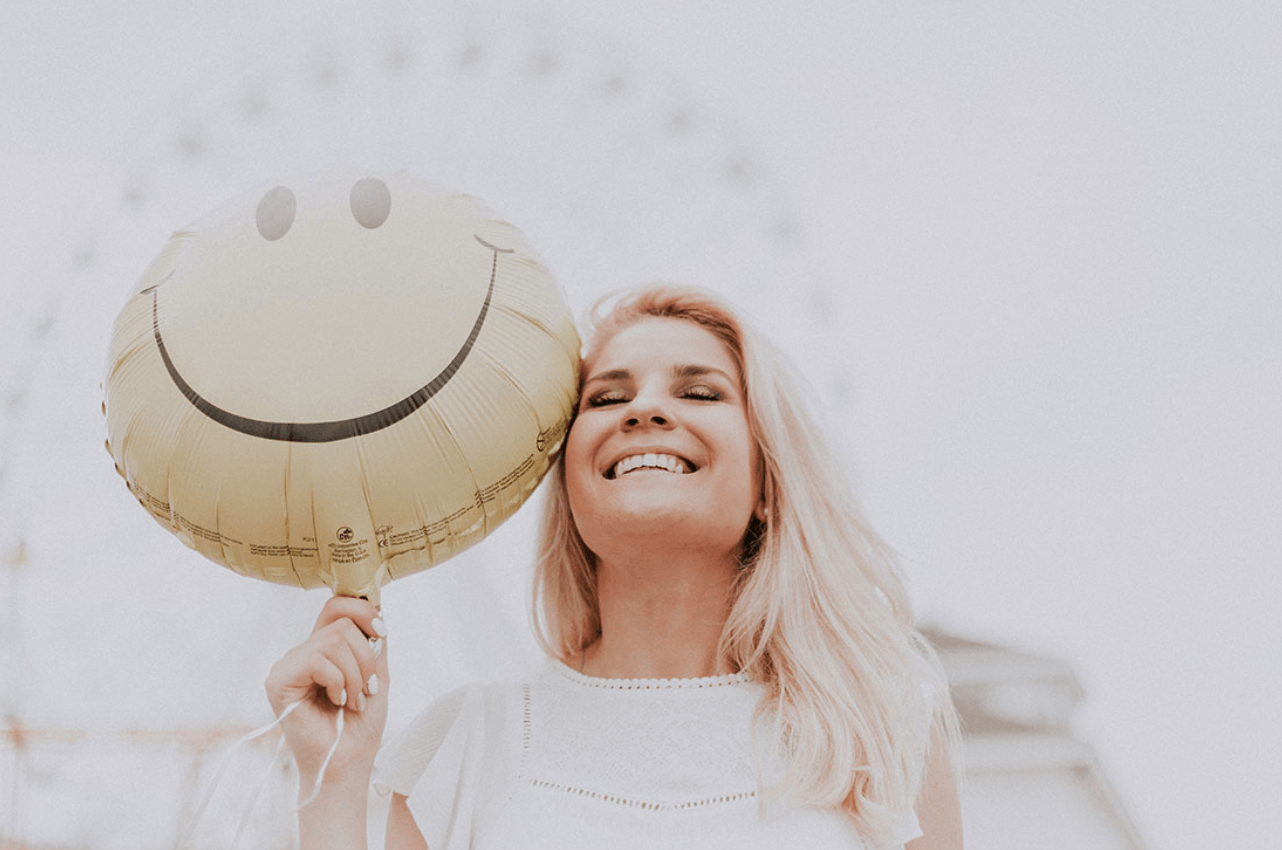 A woman is holding a smiley face balloon in front of her face.