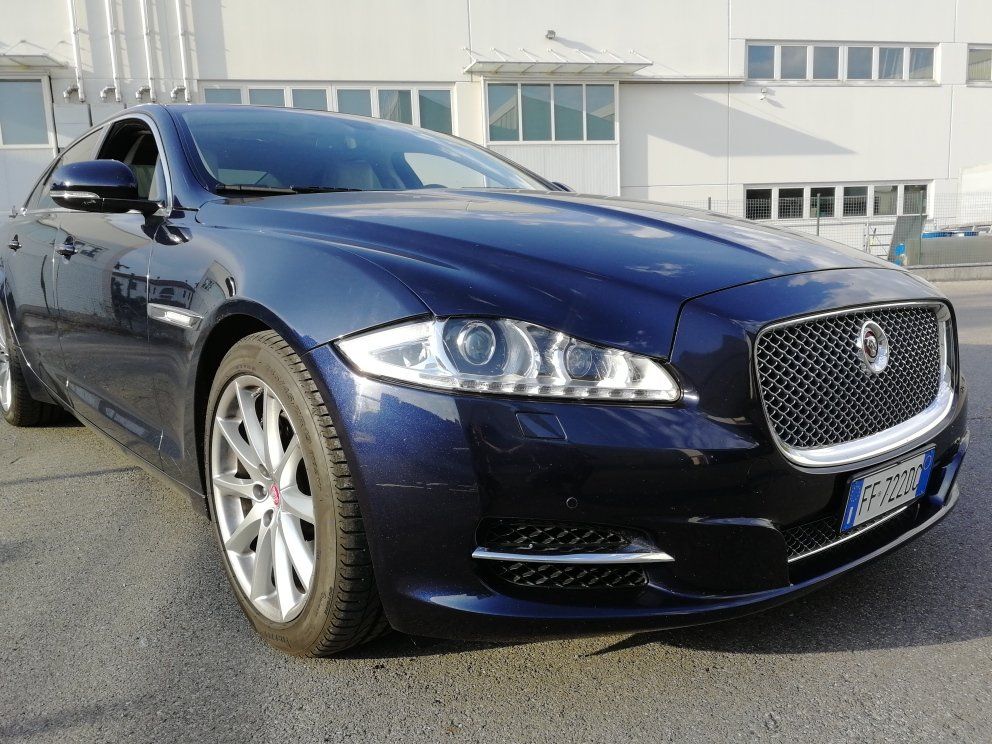 Una berlina Jaguar blu scuro parcheggiata davanti a un edificio.
