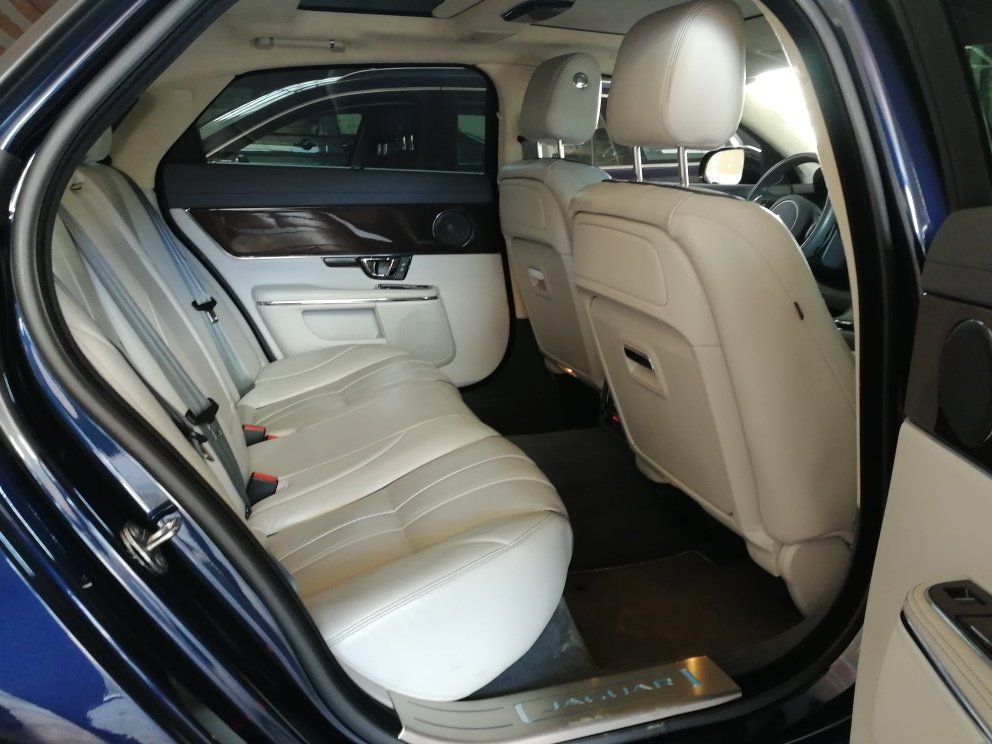 Vista dell'interno di una Jaguar blu, con sedili in pelle beige e finiture in legno.