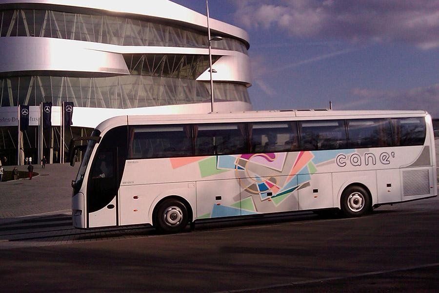 Autobus bianco dal design colorato di fronte a un edificio moderno con facciata in vetro arrotondata.