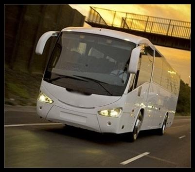 Autobus bianco che percorre una strada sotto un ponte; sullo sfondo un tramonto dorato.