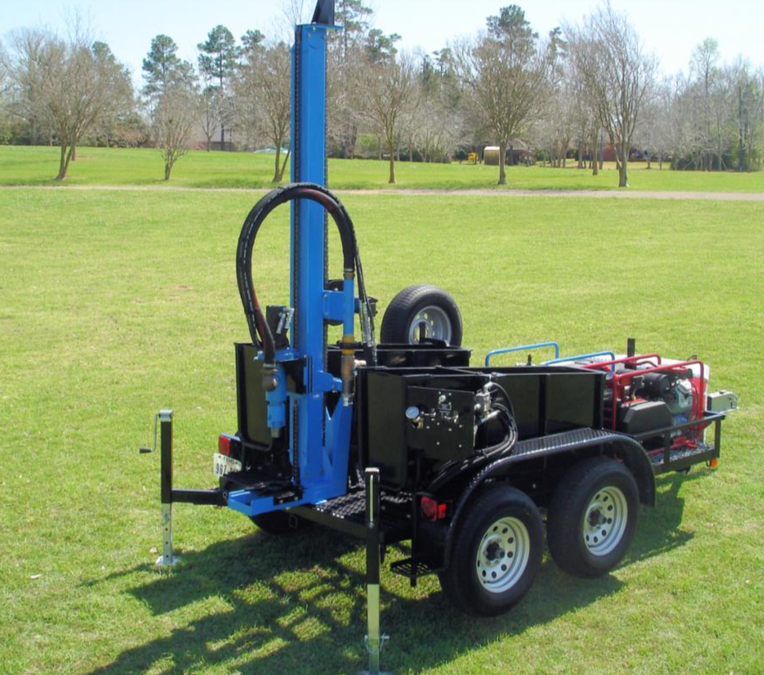 A trailer with a drill on it is parked in a grassy field