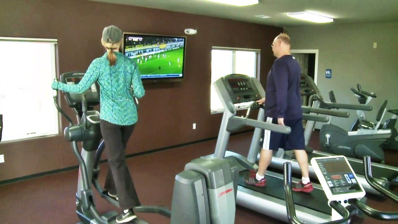 A woman is riding an elliptical while a man is running on a treadmill in a gym.
