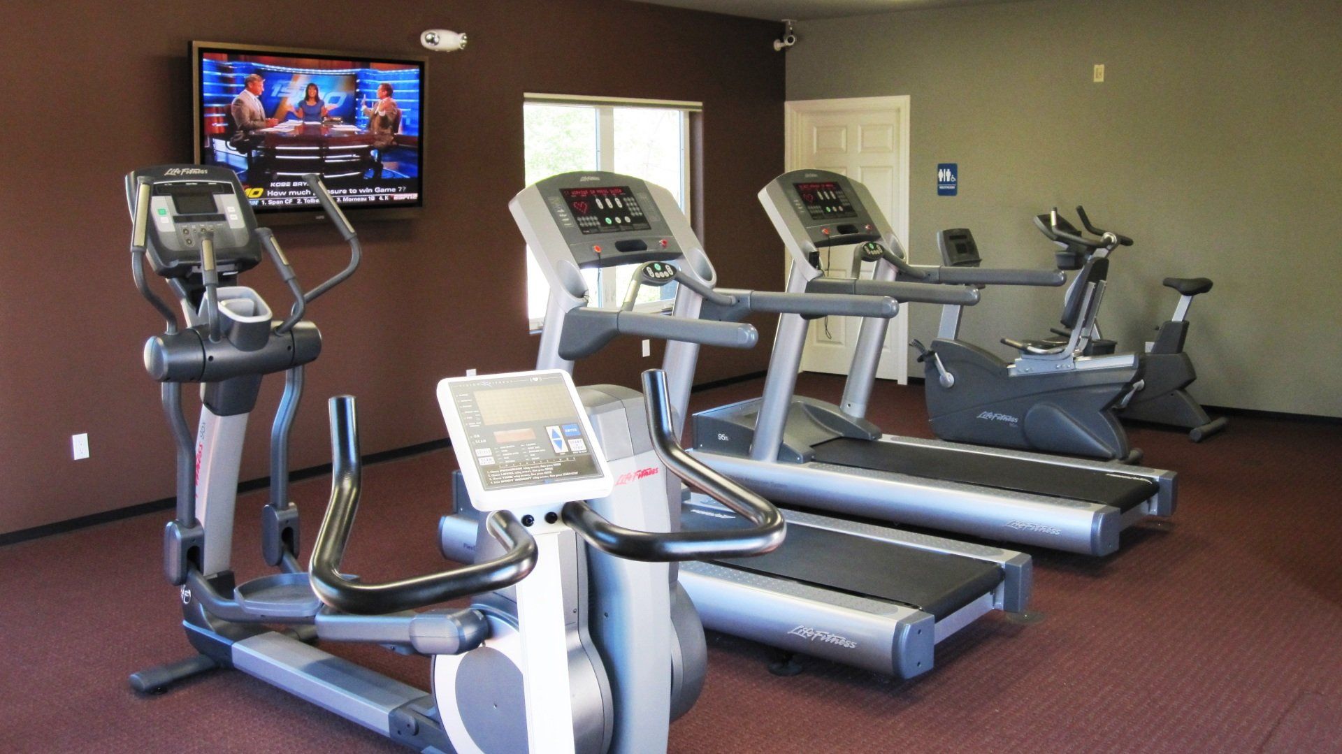 A gym with treadmills , ellipticals and a television on the wall