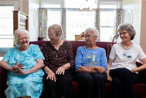 Four elderly women are sitting on a couch and laughing