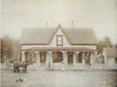 A black and white photo of a house with a horse in front of it