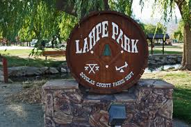 A large wooden sign is sitting on top of a stone wall in a park.