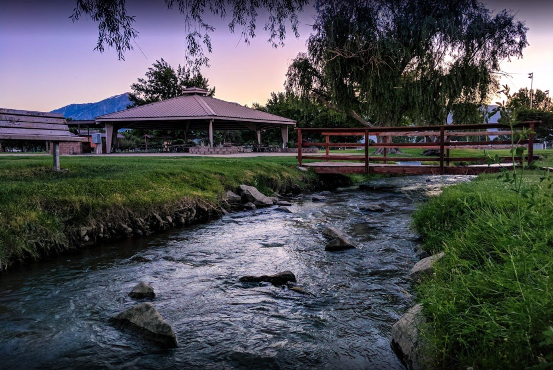 A bridge over a river in a park with a pavilion in the background.