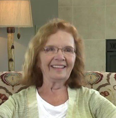 A woman wearing glasses is smiling while sitting on a couch.