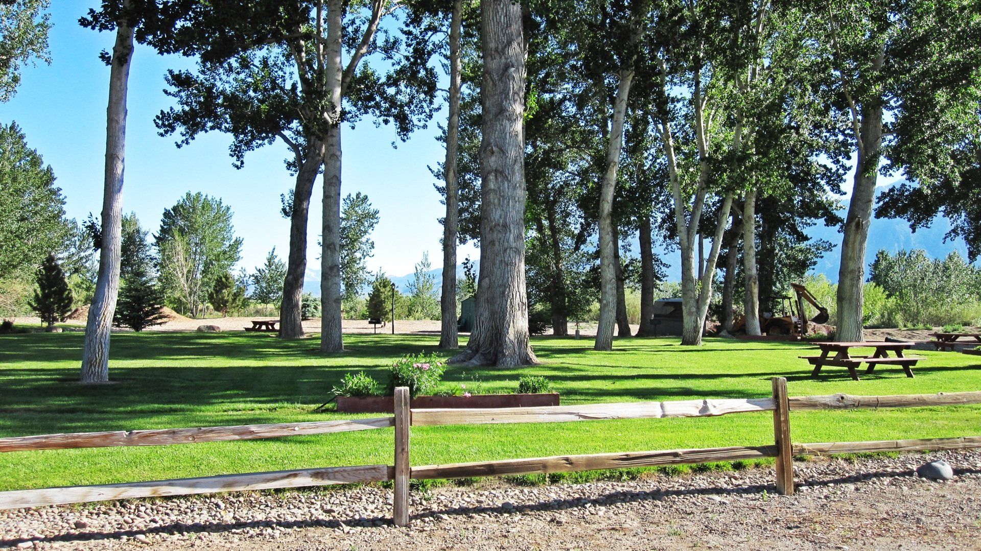 A wooden fence surrounds a picnic area with trees in the background