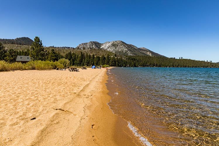 A sandy beach next to a lake with mountains in the background.