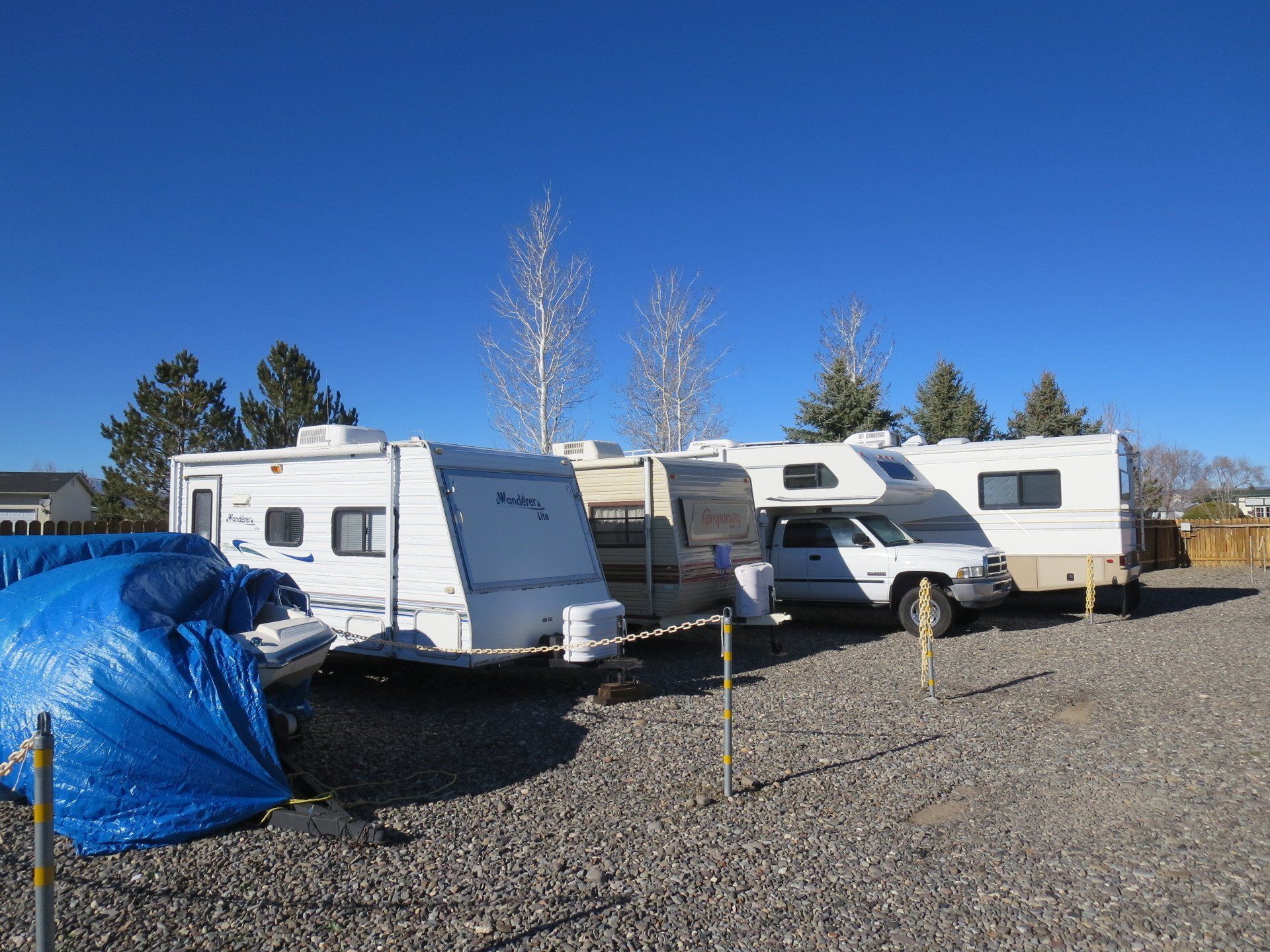 A row of rvs are parked in a gravel lot
