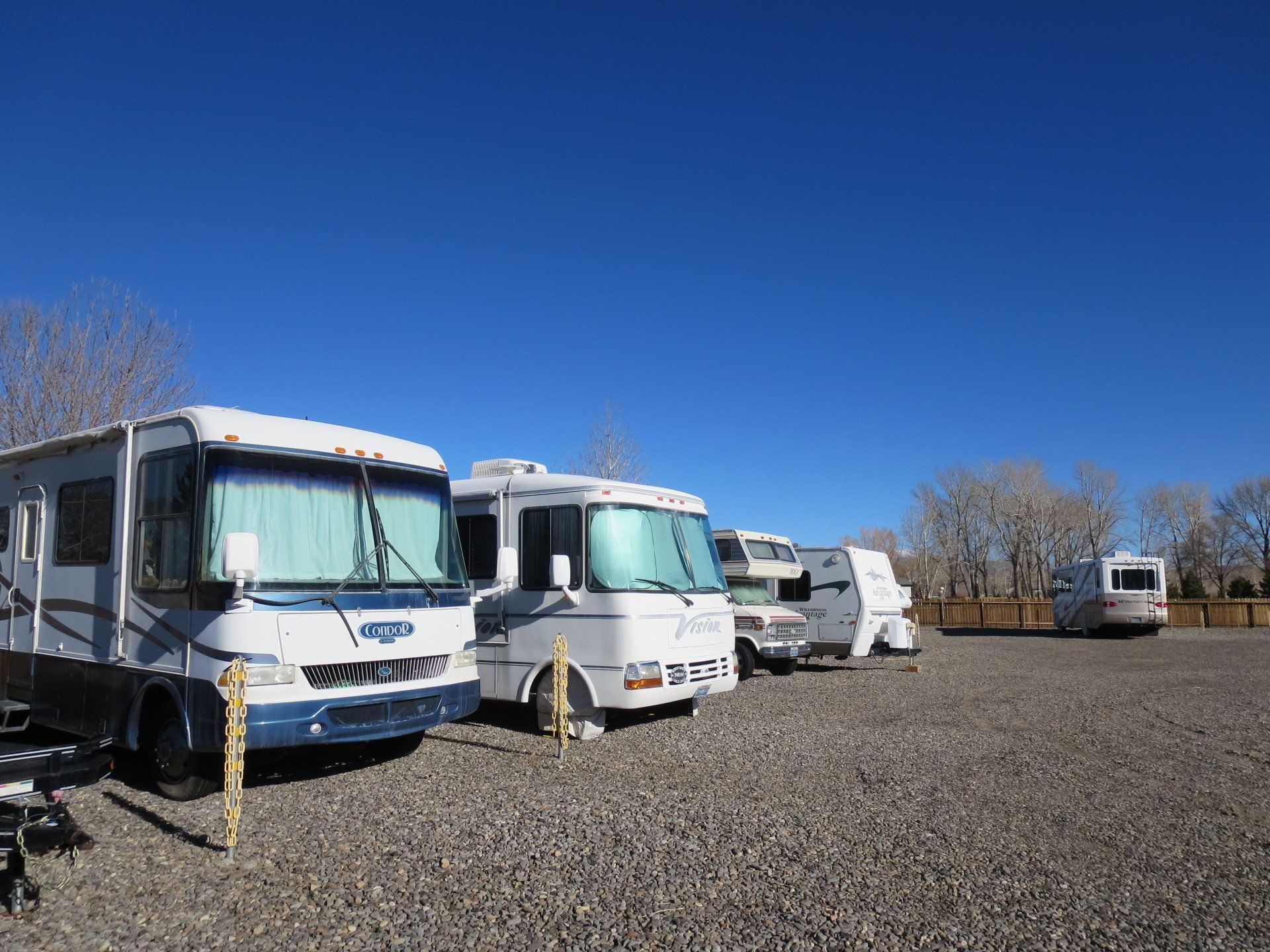 A row of recreational vehicles are parked in a gravel lot.