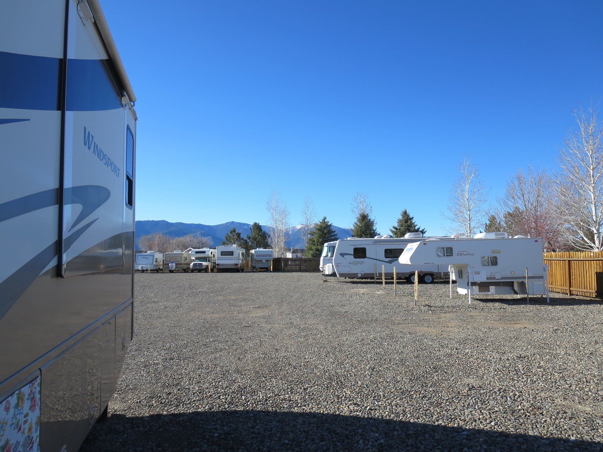 A row of rvs are parked in a gravel lot