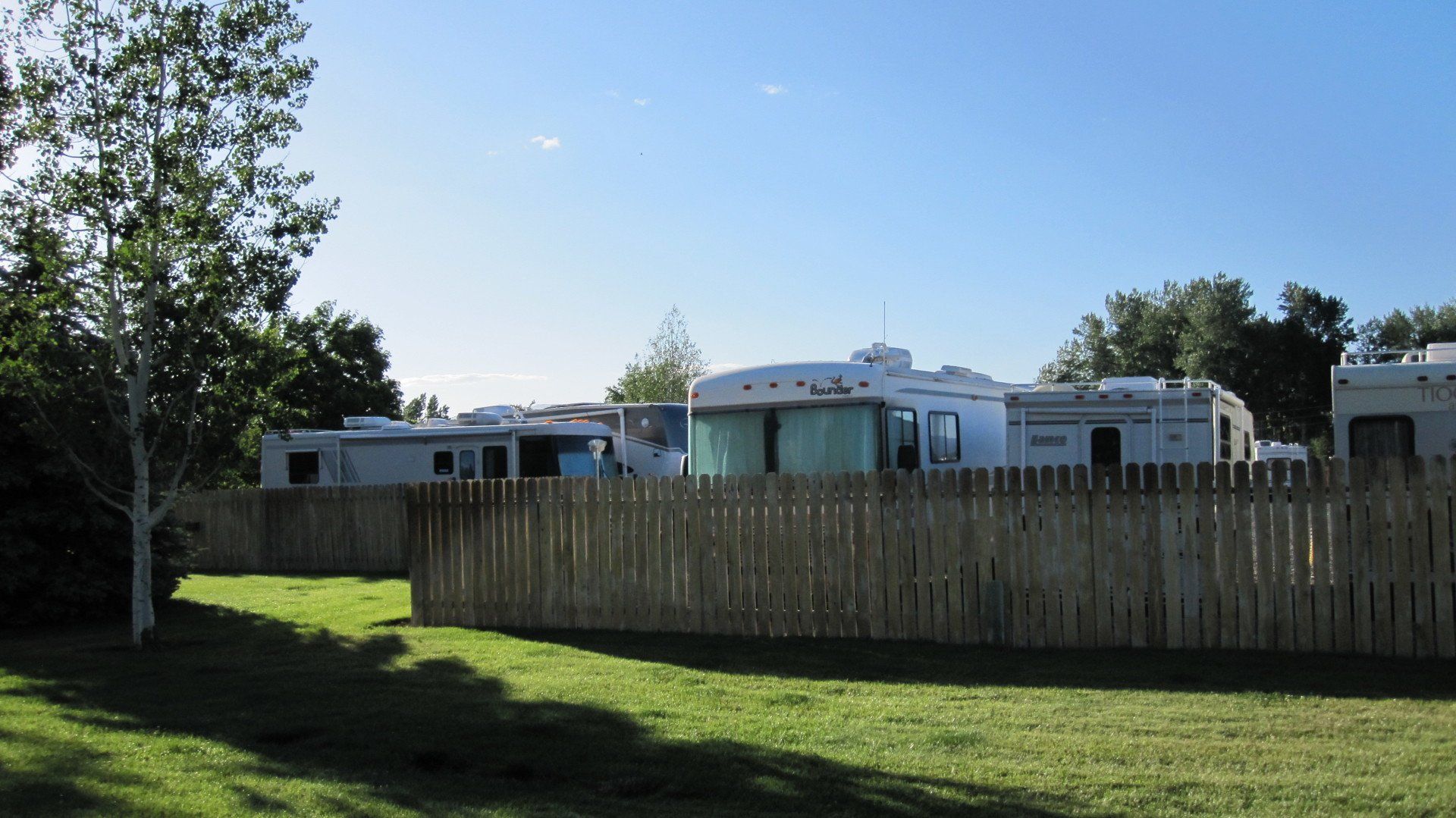 A wooden fence surrounds a grassy field with a few rvs in the background