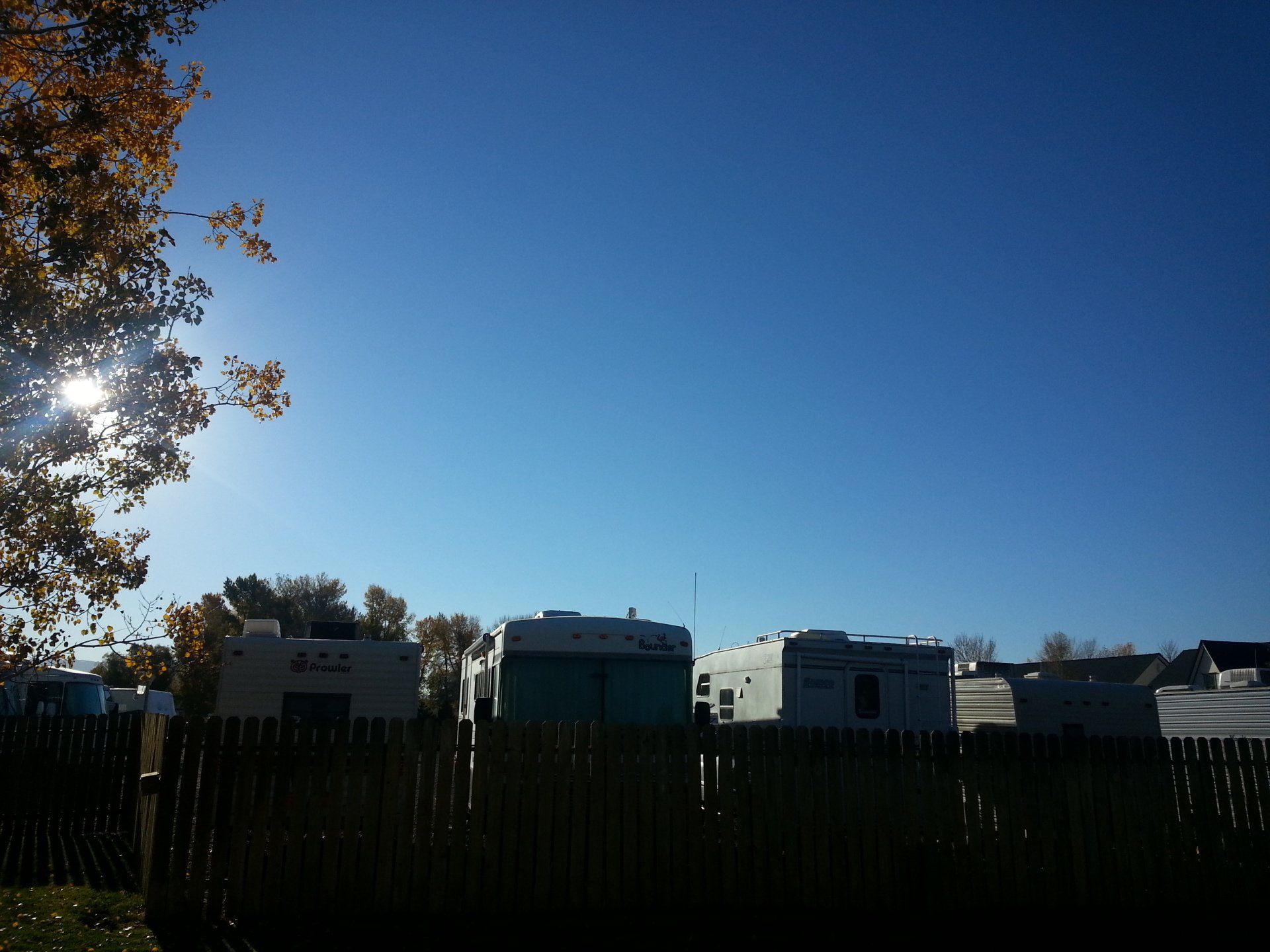 A row of rvs are parked behind a wooden fence