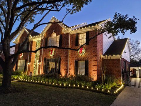 A large brick house is decorated with christmas lights and a wreath.