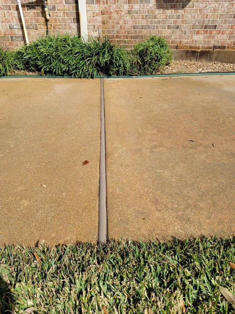 A concrete sidewalk with a brick wall in the background and grass in the foreground.
