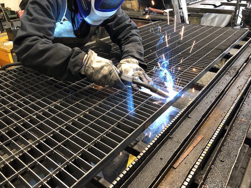 Un operaio salda una griglia metallica, con scintille blu brillanti, in un'officina industriale.