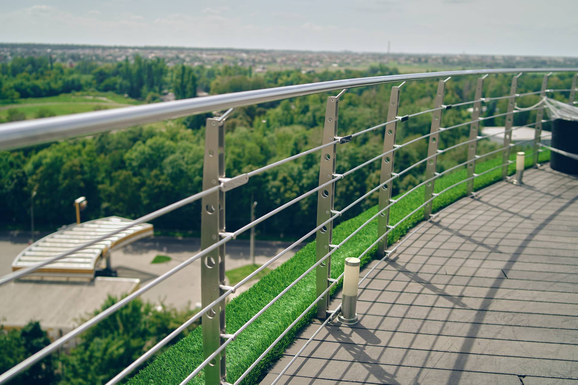 Terrazza sul tetto con ringhiera in vetro che si affaccia su un paesaggio verdeggiante e sull'autostrada in una giornata di sole.
