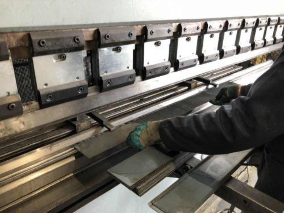 Operaio che maneggia lamiere metalliche su una pressa piegatrice in un'officina metallurgica.