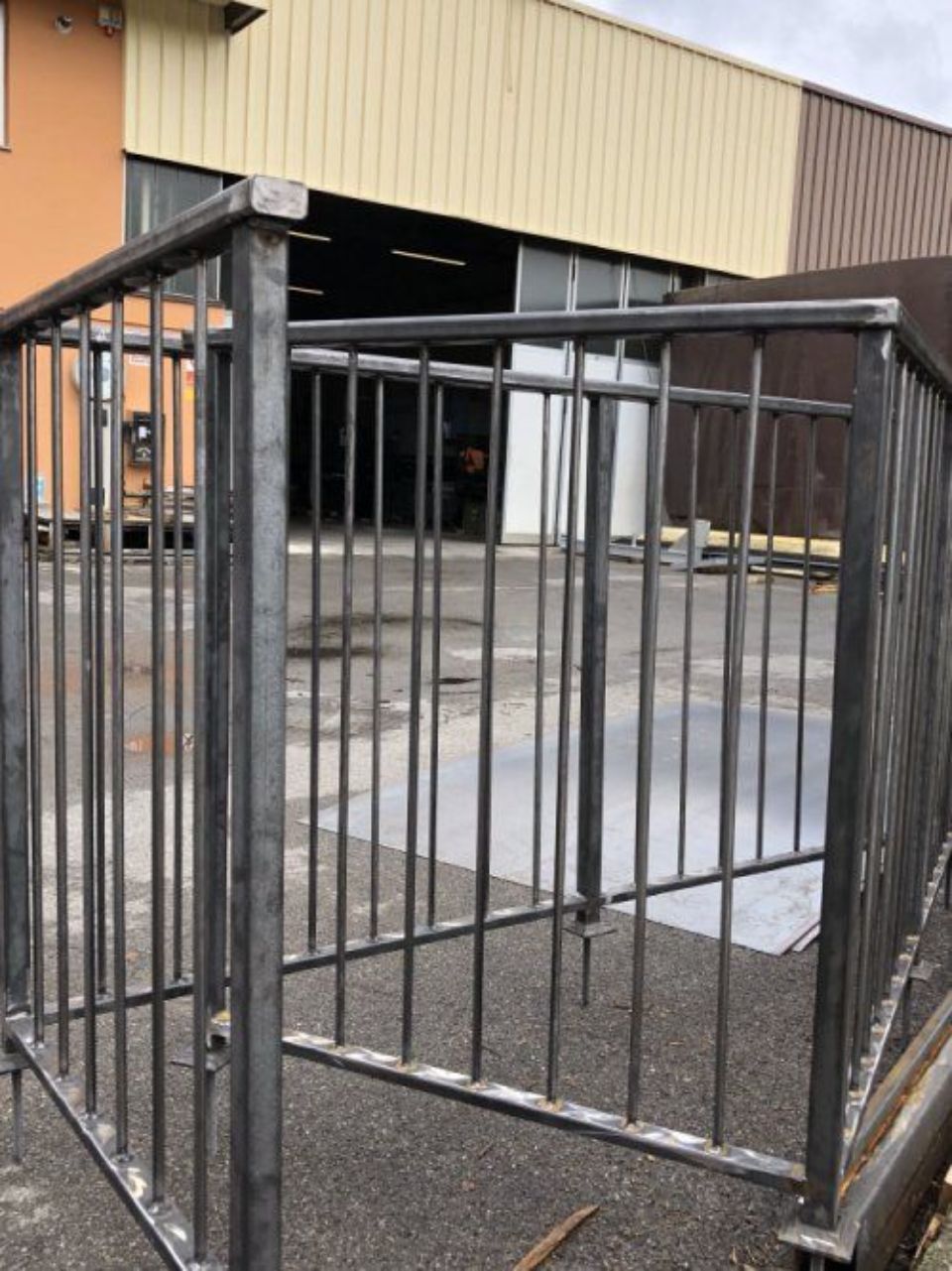 Cancello di sicurezza in metallo con sbarre verticali all'esterno di un edificio industriale su un piazzale pavimentato.