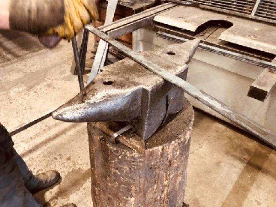 In un'officina, un'incudine da fabbro è appoggiata su un ceppo di legno, con una persona in piedi nelle vicinanze.