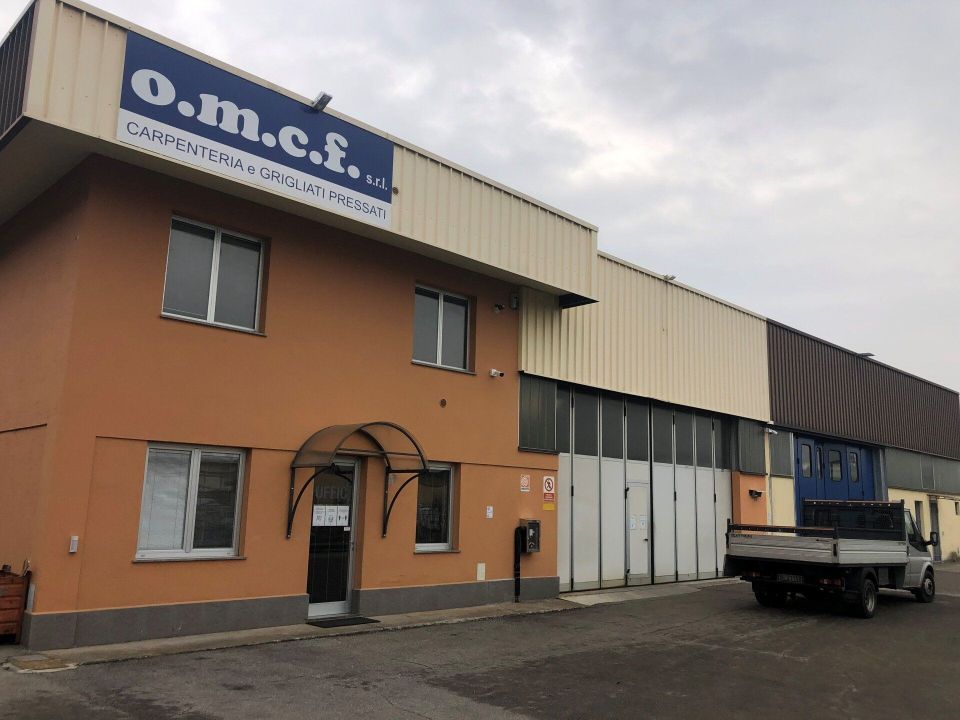 Edificio industriale con insegna OMCS, facciata arancione e grigia e un camion parcheggiato all'esterno.