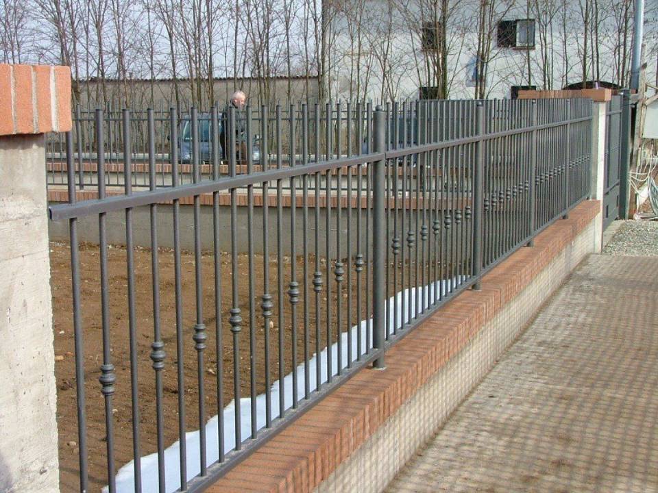 Recinzione metallica con sbarre verticali accanto a un muro di mattoni lungo un marciapiede in un'area esterna