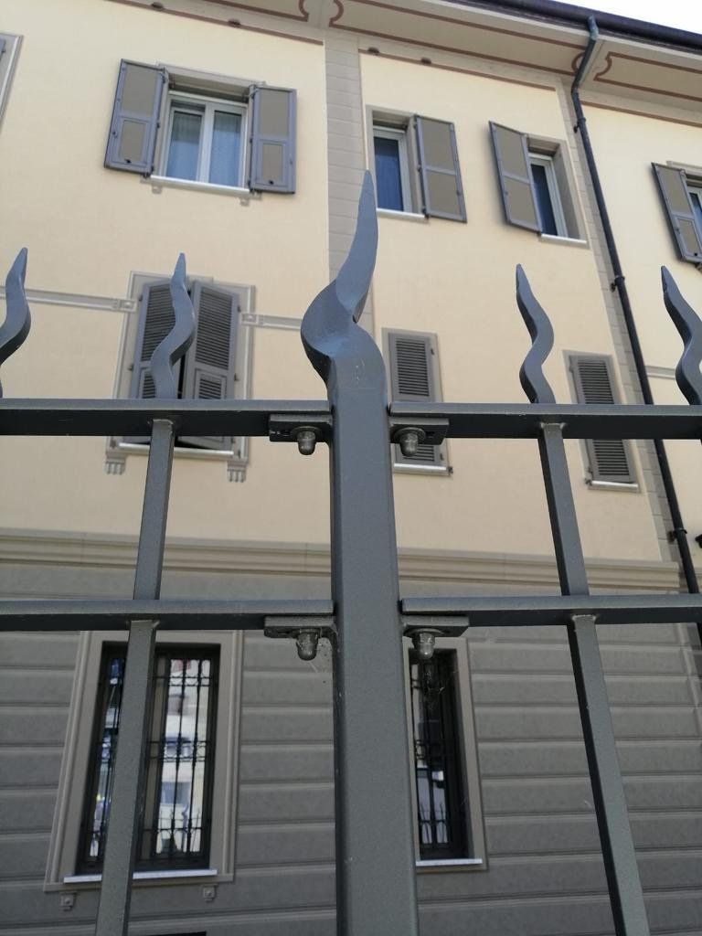 Facciata beige dell'edificio con finestre aperte dietro una recinzione metallica nera con punte ondulate.