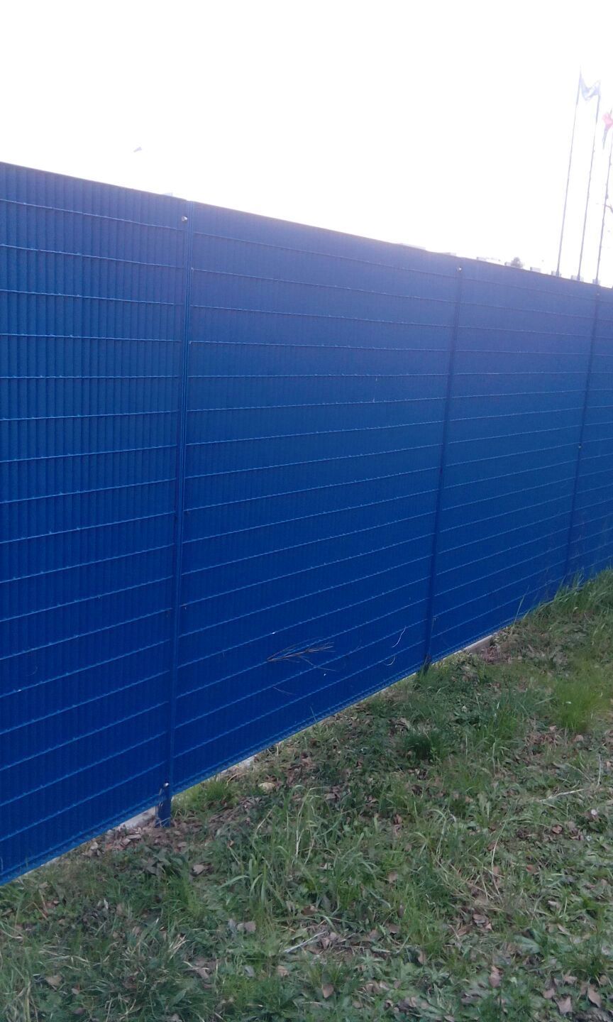 Una recinzione di tegole blu lungo un ciglio erboso della strada, sotto la luce del giorno.