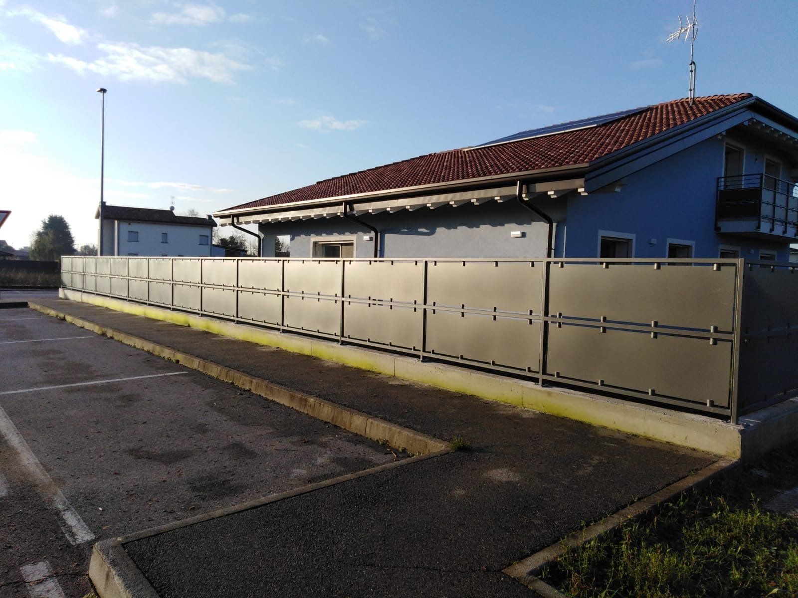 Casa residenziale con recinzione beige e tetto di tegole rosse accanto a una strada lastricata al tramonto