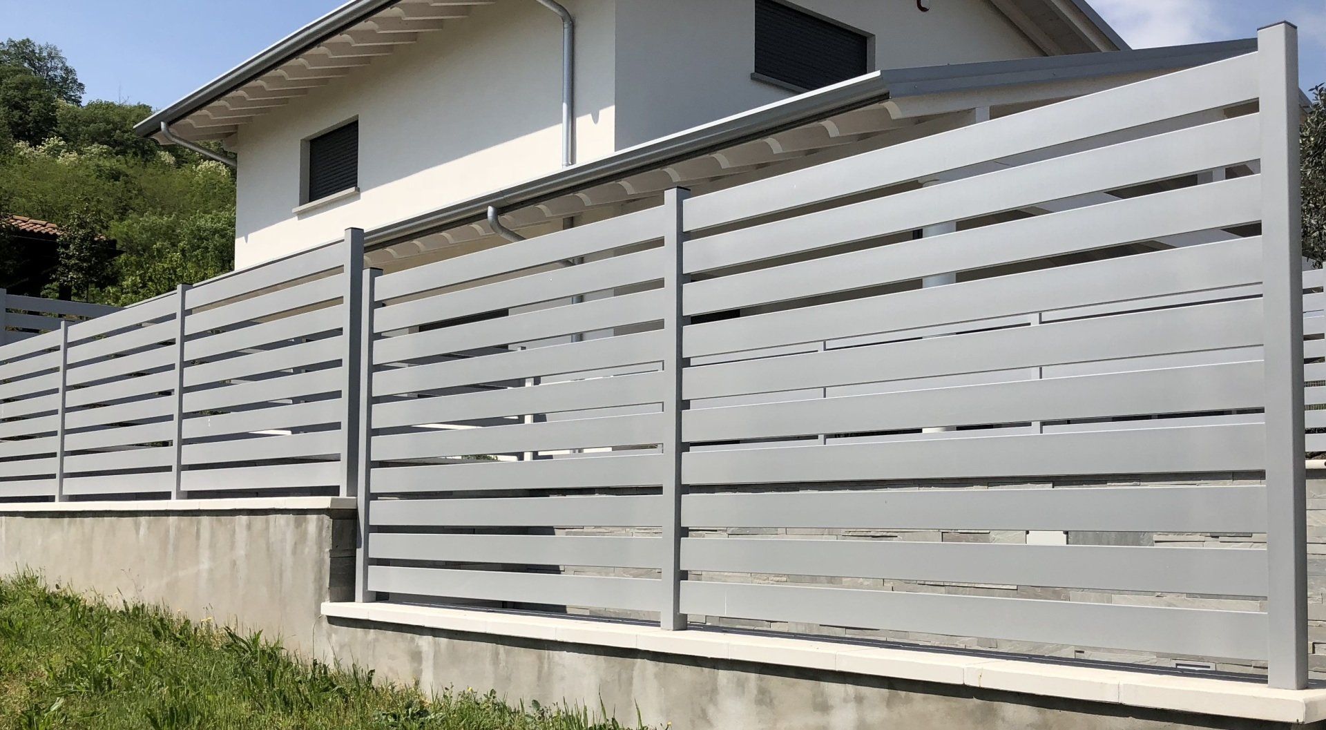 Moderna recinzione bianca a doghe orizzontali lungo un muro di cemento accanto a una casa e a un cortile erboso.