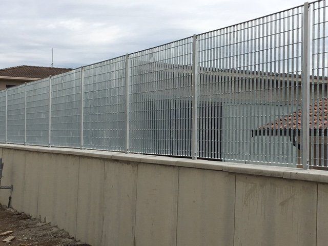 Alta recinzione metallica di sicurezza lungo un muro di cemento accanto a un edificio
