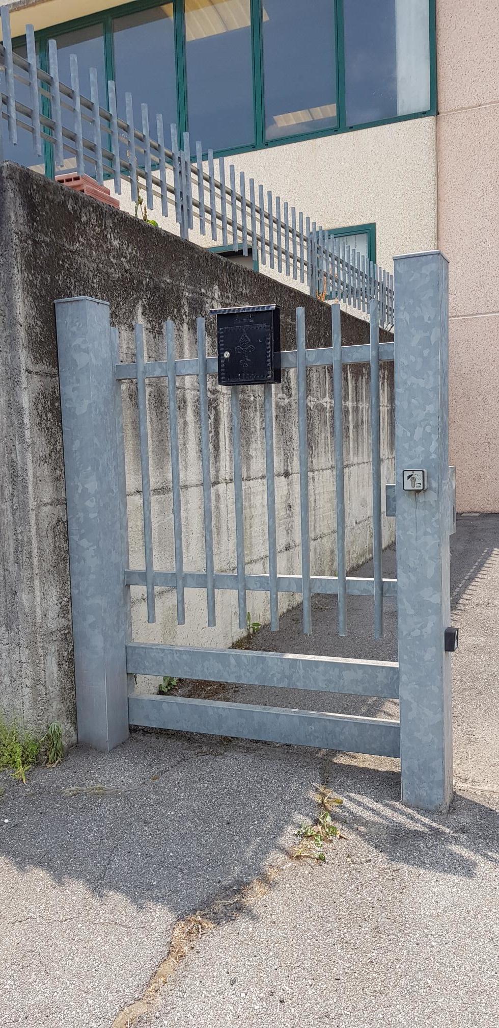 Cancello metallico blu accanto all'ingresso di un edificio e muro di cemento su un sentiero di ghiaia