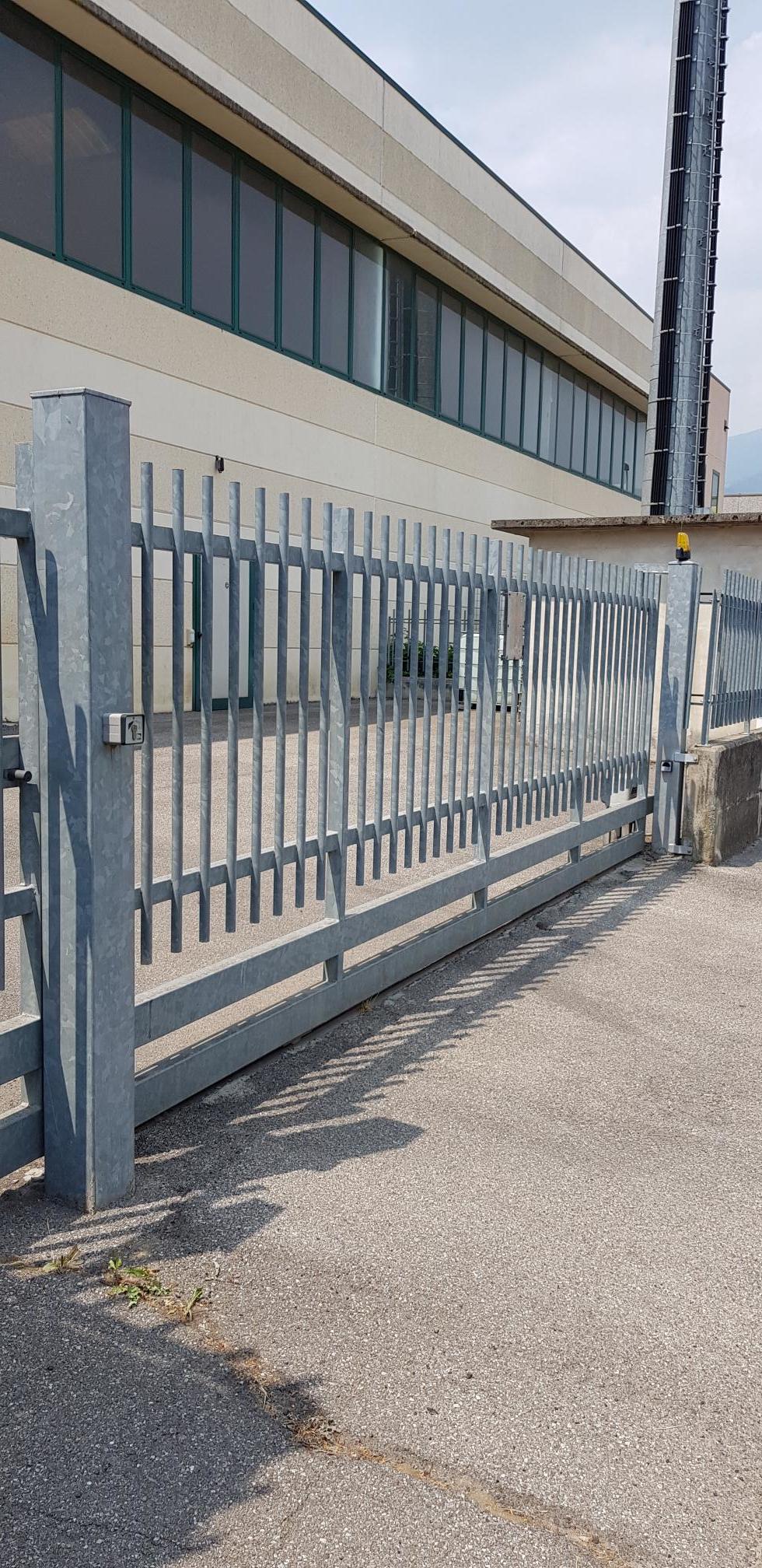 Recinzione e cancello in metallo accanto a un edificio beige su un marciapiede soleggiato.
