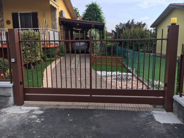 Cancello carrabile in metallo marrone davanti a una casa con un sentiero in pietra e un prato verde.