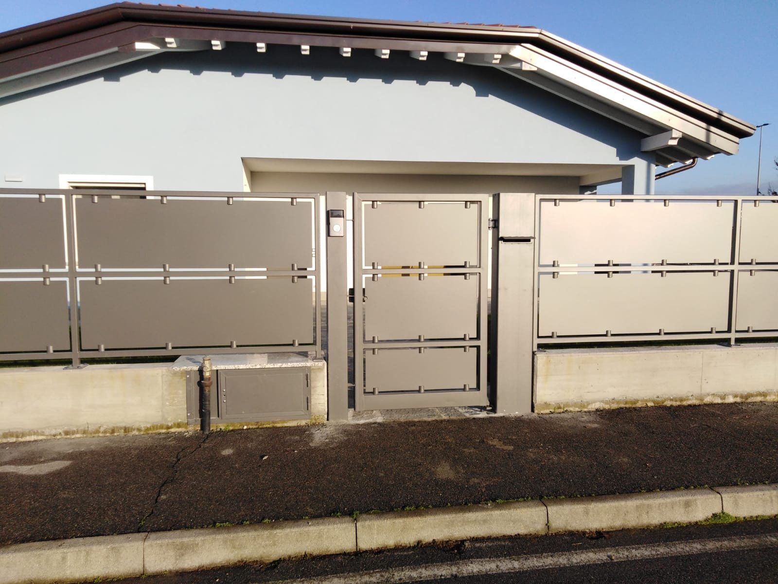 Cancello e recinzione in metallo beige davanti a una casa sotto un cielo limpido
