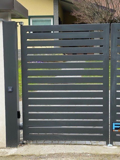 Cancello in metallo grigio scuro con doghe orizzontali all'ingresso di una casa moderna.