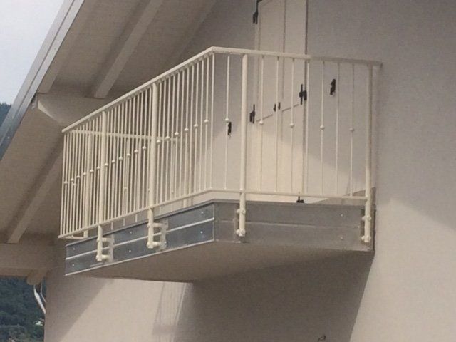 Ringhiera di un balcone in metallo bianco, fissata alla facciata di un edificio sopraelevata rispetto alla strada.