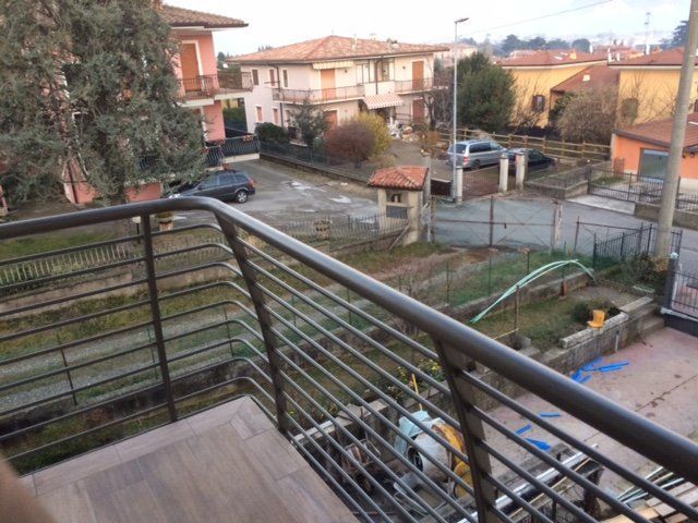 Vista dal balcone su una strada residenziale e sulle case, con ringhiera metallica in primo piano.