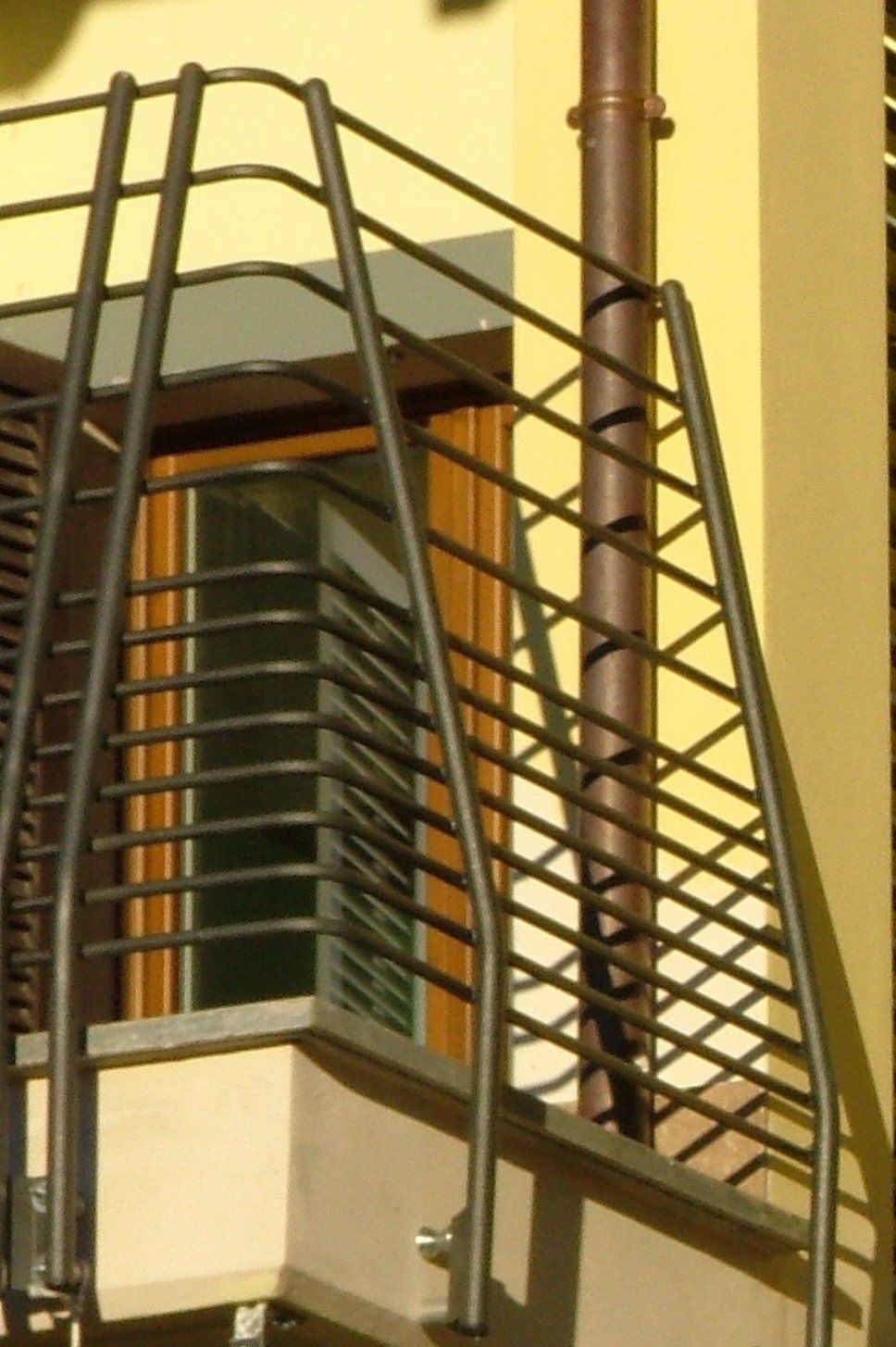 Balcone di un edificio giallo con ringhiere in metallo nero e una finestra alle sue spalle.
