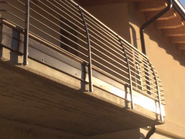 Ringhiera metallica di un balcone sulla facciata di un edificio, illuminata da una calda luce solare.
