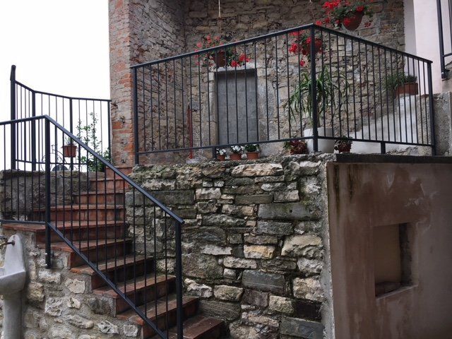 Scala in pietra accanto a un muro rustico con ringhiere in metallo nero e fiori rossi su una terrazza