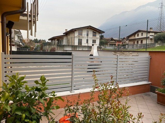 Balcone con ringhiera in metallo grigio, piante in vaso e vista su case e montagne.